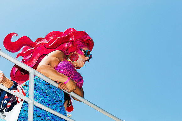 Drag performer in vibrant costume descending a ferry during the annual Invasion of the Pines celebration on Fire Island, photographed by Koitz.