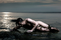 A nude figure reclines on shoreline rocks at Great South Bay, Fire Island, during dusk, with calm water and soft evening light creating a serene coastal scene.