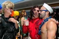 A person in a sailor hat shares a warm embrace with a friend in a red sequined outfit during the Invasion of the Pines celebration in Cherry Grove, surrounded by colorful attendees.