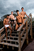 Four friends pose on wooden beach access stairs at Fire Island, wearing swimwear and smiling during a summer portrait against a dramatic coastal sky.