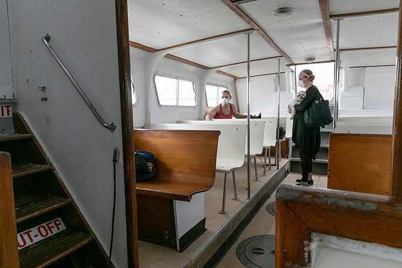 Passengers board and travel on a special ferry from Sayville to Fire Island during the COVID-19 pandemic, documenting the unusual transportation arrangements, reduced capacity, protective measures, an