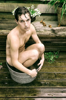 A nude man sitting in a galvanized metal tub on a wooden deck in Cherry Grove, Fire Island, looking toward the camera in a fine art portrait.