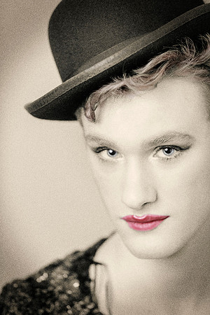 Close-up portrait of Ian wearing a black hat and sequined top, with red lipstick, photographed by koitz.