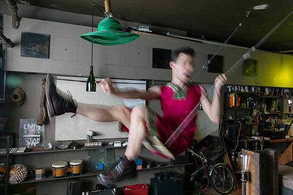 koitz photograph of Brock wearing a dress and seated on a swing, capturing a playful and theatrical moment within Fire Island’s queer visual culture.