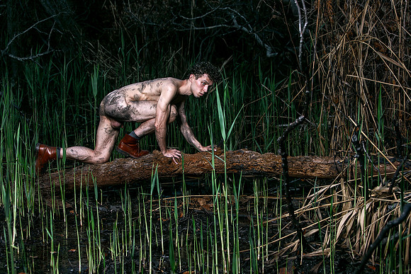 Brock kneeling on a burnt branch among the charred trees of the Meat Rack on Fire Island, photographed by koitz.