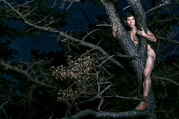 Brock looks through two charred branches in the Meat Rack on Fire Island, photographed by koitz as part of his queer fine-art photography series.